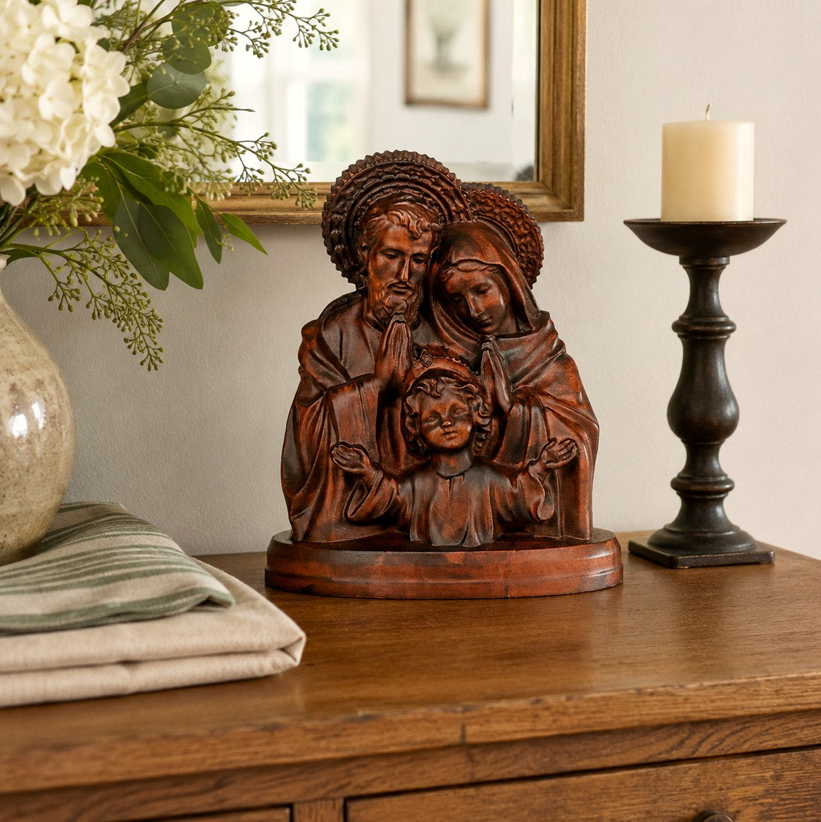 Carved wooden Holy Family statue of Jesus, Mary and Joseph on a sideboard beside a candle