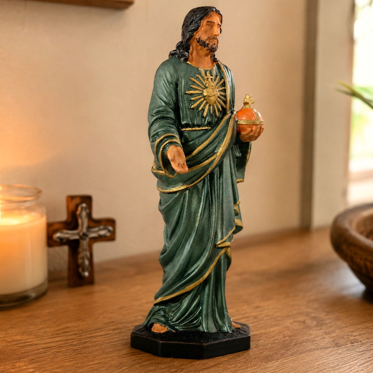 Hand-painted Sacred Heart of Jesus statue in teal and gold, displayed on a wooden console beside a lit candle