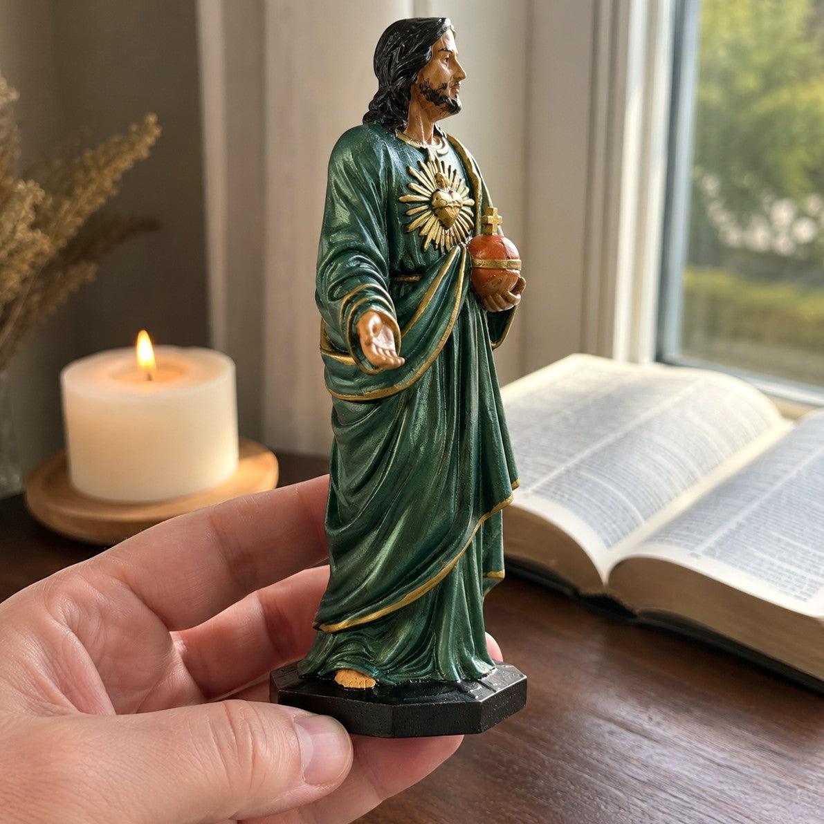 Hand-painted Sacred Heart statue held in one hand, showing its true size beside an open book