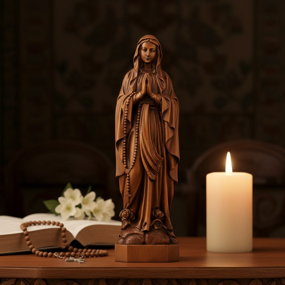 Carved beechwood Our Lady of Lourdes statue on a home altar with a lit pillar candle and white flowers