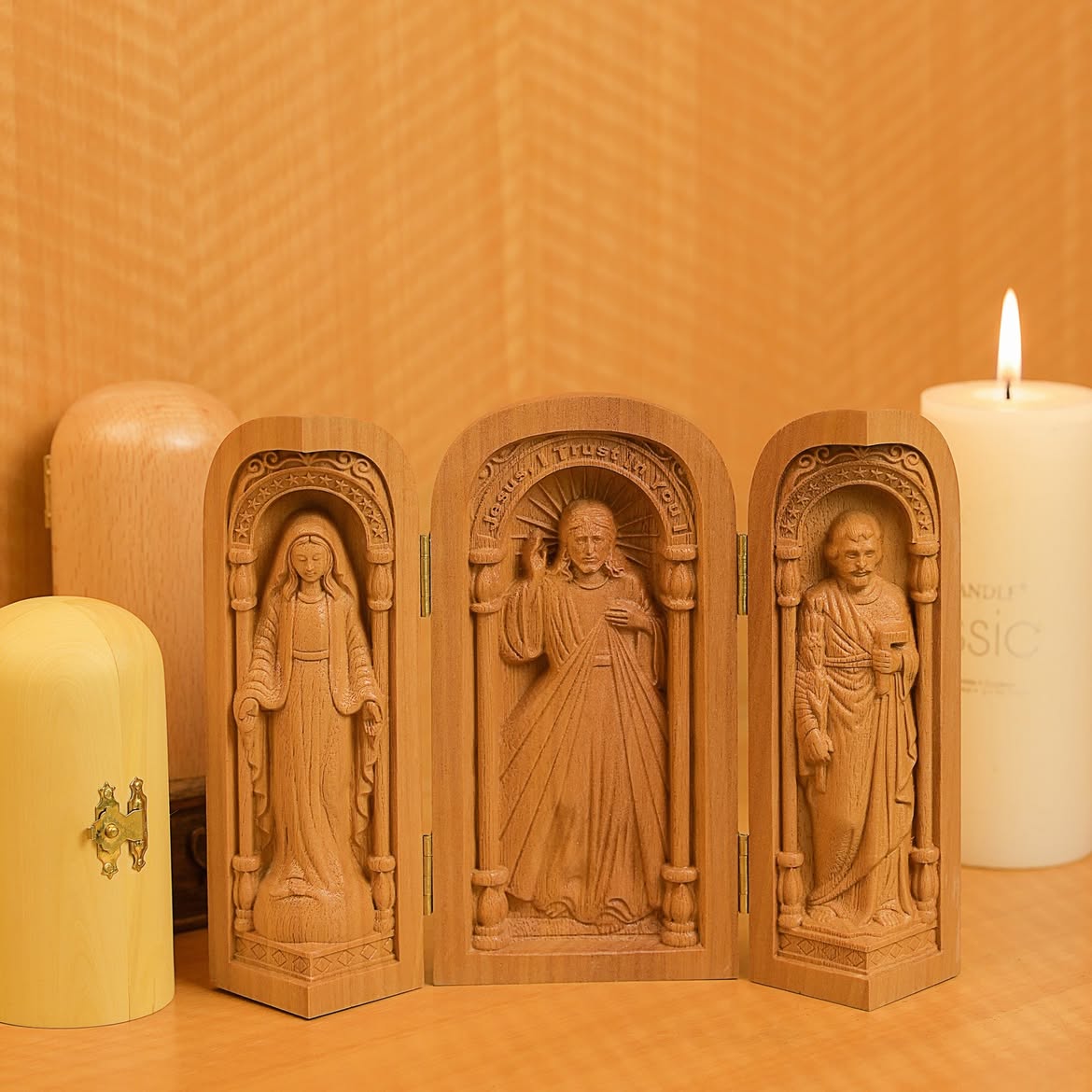 Travel triptych altar open on a table beside a candle, with its closed capsule form alongside