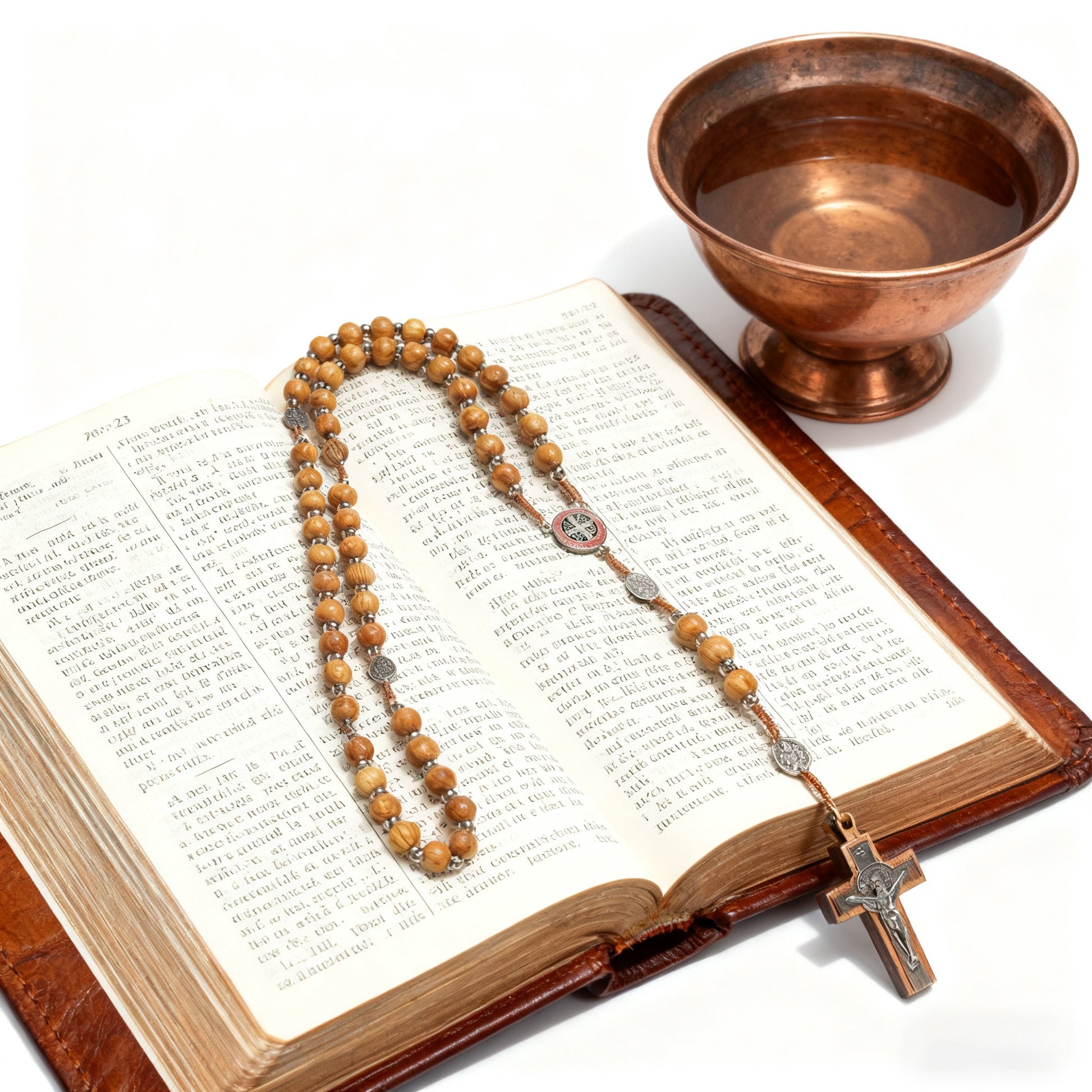The rosary laid across an open bible beside a copper bowl