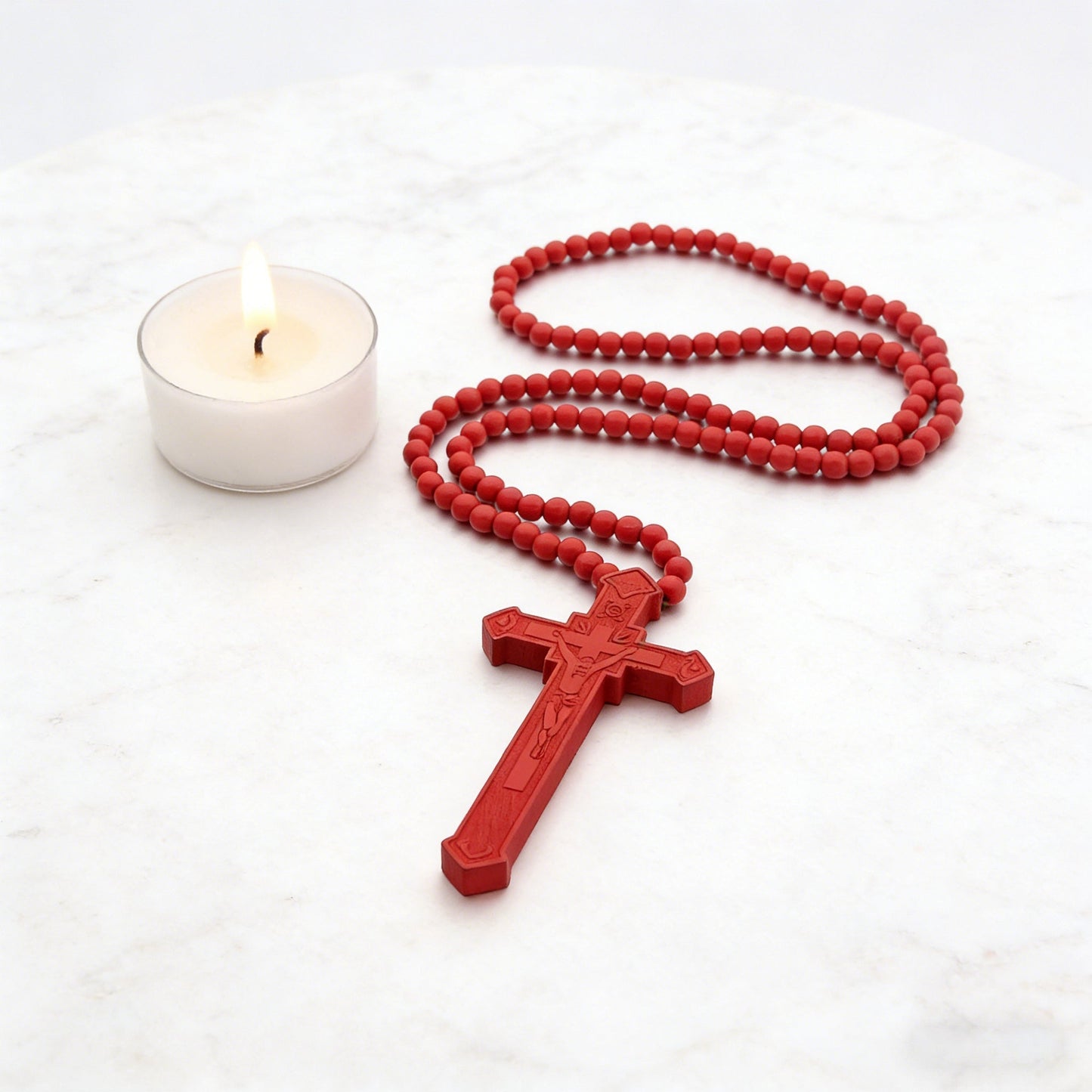 Red wooden bead rosary beside a lit candle