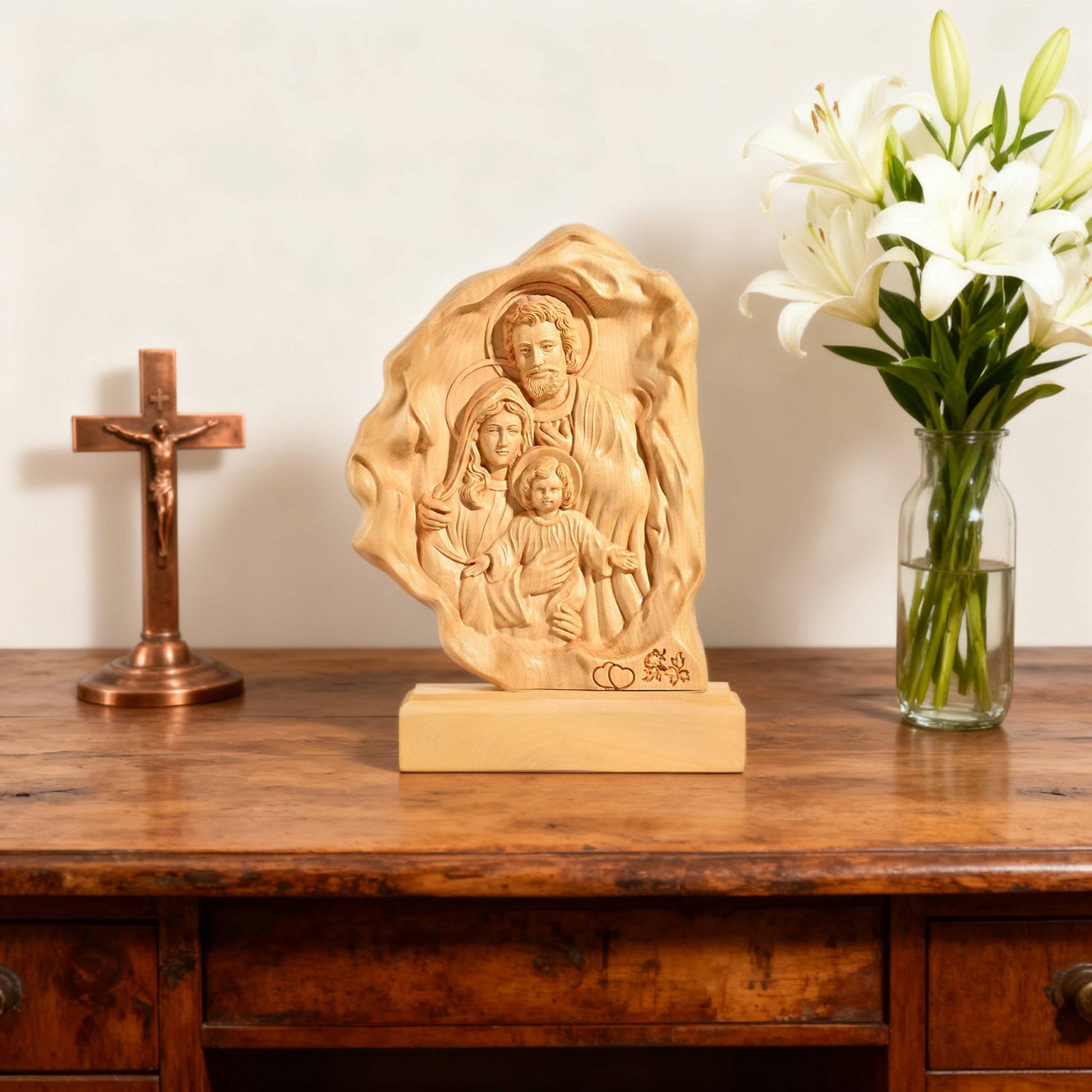 The boxwood Holy Family relief on a table beside a crucifix and lilies
