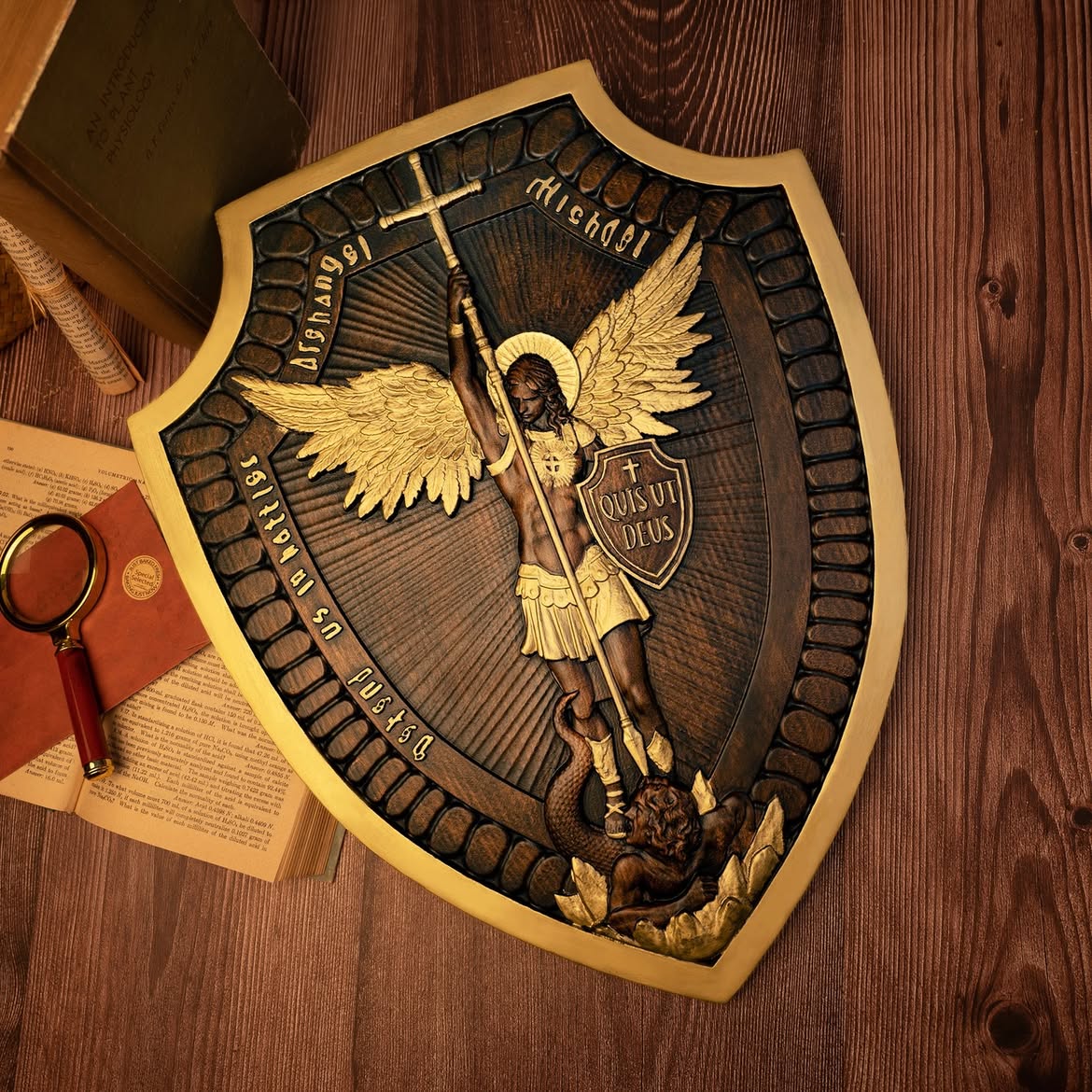 Archangel Michael shield carving with gold detail lying on a wooden floor beside old books